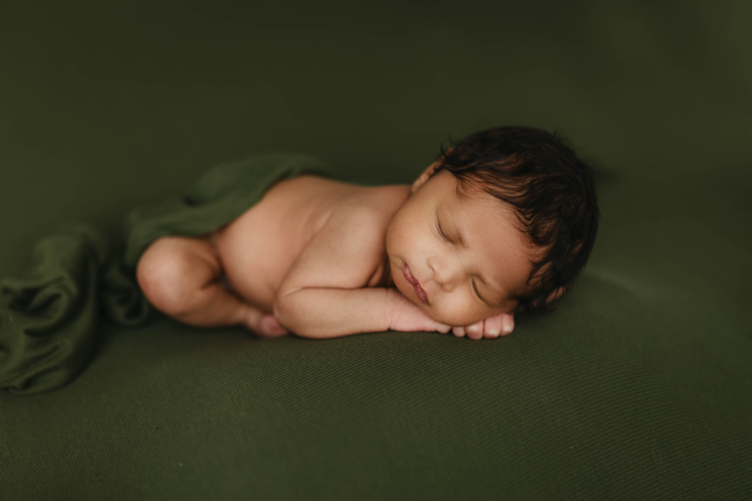 A peaceful sleeping newborn on green fabric background.
