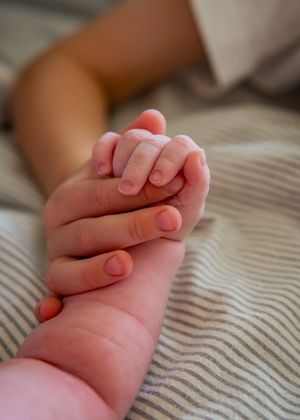 Close-up shot of baby's small hand holding adult fingers against striped fabric.