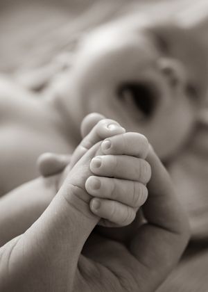 Close-up black and white photograph of a baby's tiny hand being held.
