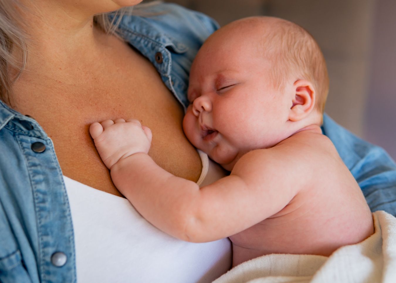 Peaceful newborn sleeping while being held against a white top and denim jacket.