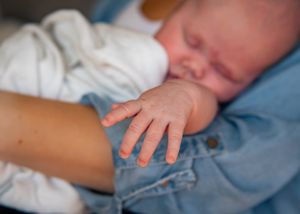 Close-up of tiny baby hand reaching out while resting in light blue fabric.