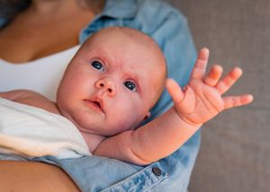 Baby with bright blue eyes and rosy cheeks resting on soft blue fabric.