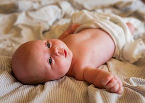 Baby lying on cream bedding looking up with bright eyes and rosy cheeks.