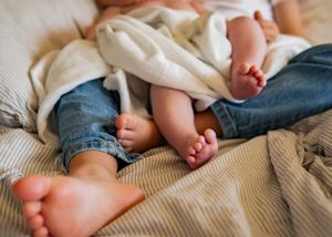 Baby feet and legs resting on textured cream bedding and denim.