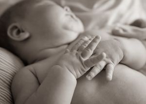 Black and white image of sleeping baby's hands resting peacefully.