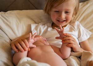 Joyful child playing and laughing while holding baby feet.