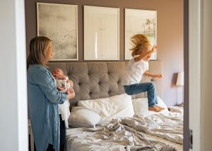 Family scene in bedroom with child jumping on gray tufted couch.