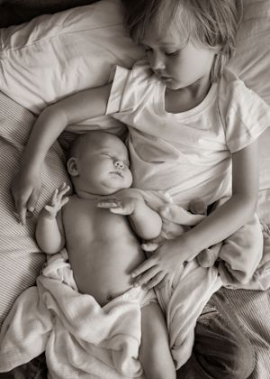 A heartwarming black and white image of siblings sharing a quiet moment together on soft bedding.
