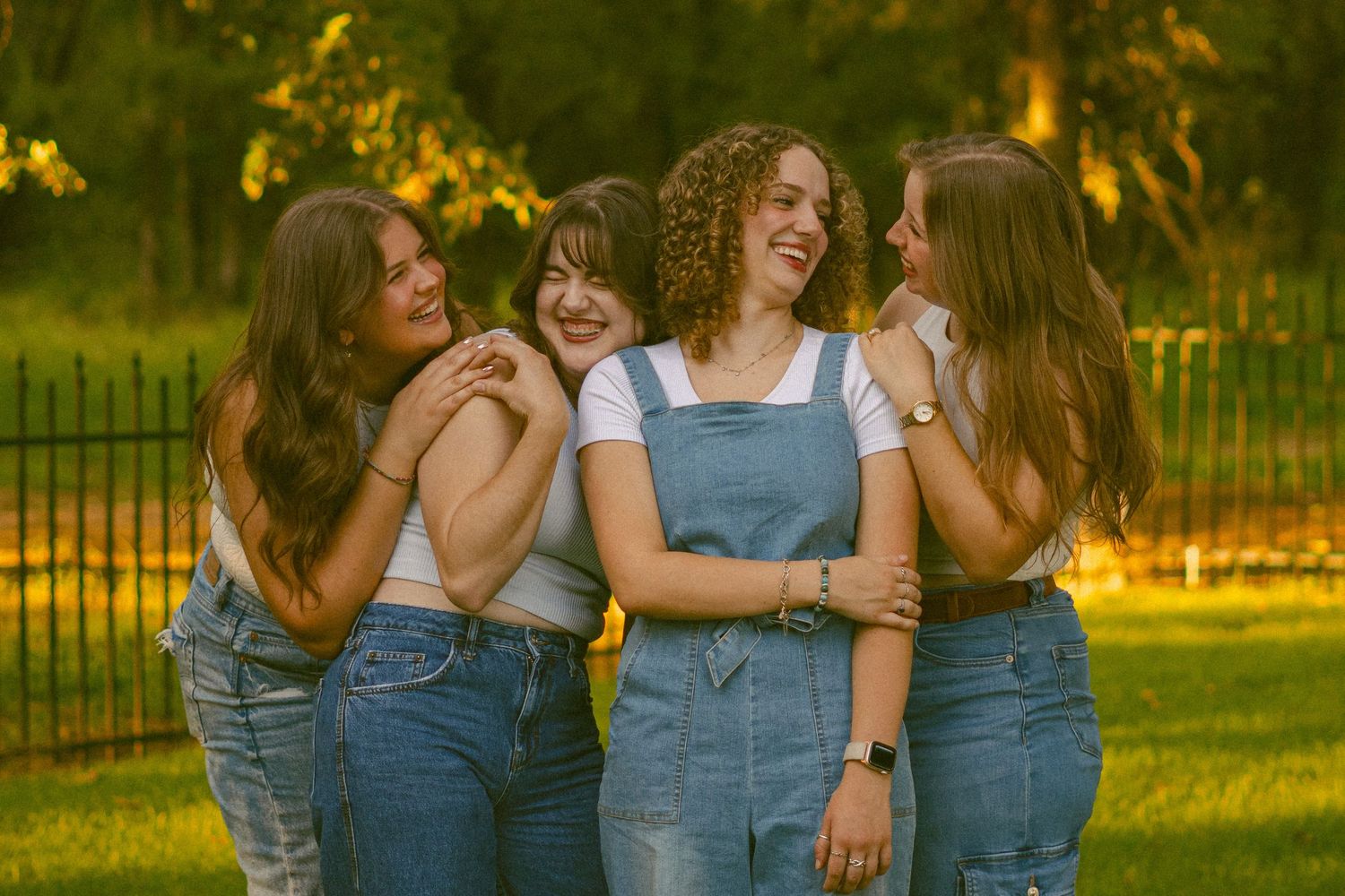 Group wearing coordinated denim overalls pose together in sunlit garden setting.