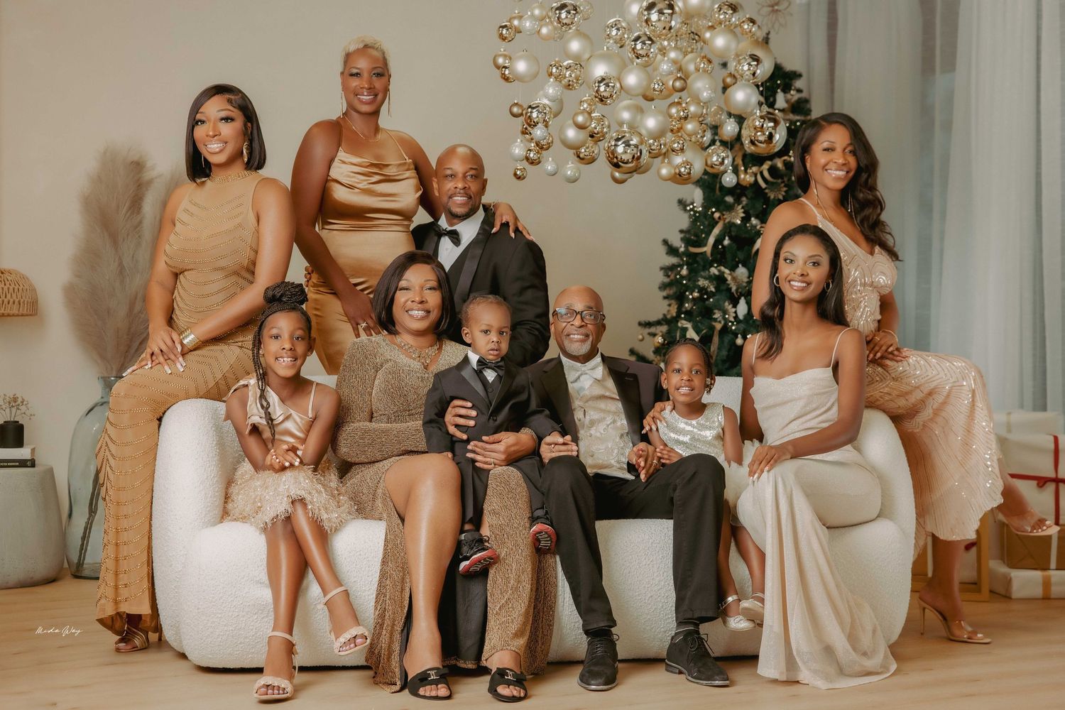 Extended family in coordinated neutral tones poses for holiday portrait with Christmas decor.