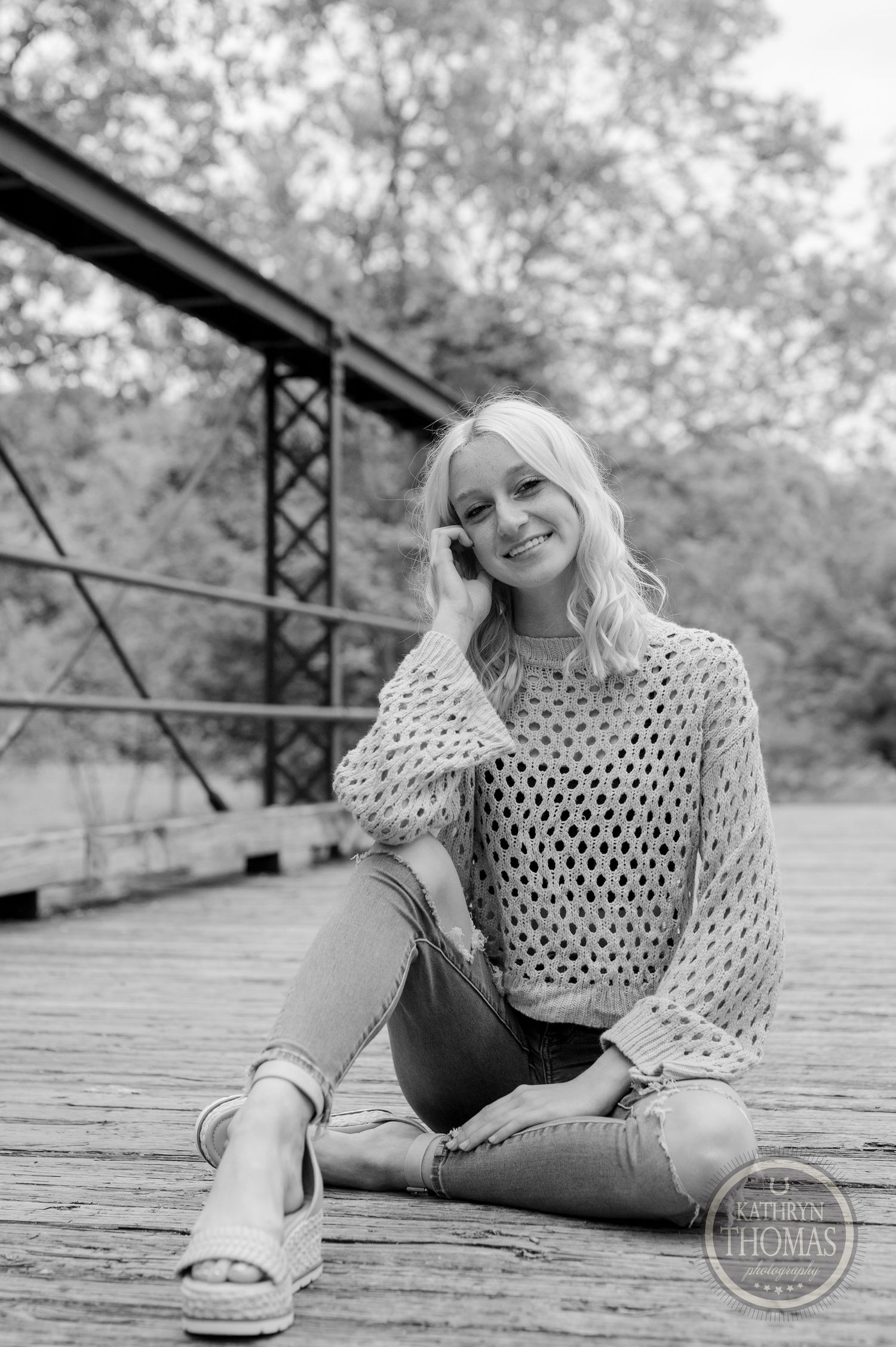 Black and white portrait sitting on wooden bridge in cream sweater and casual denim.