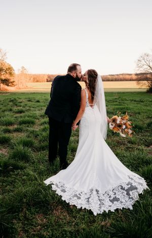 Romantic sunset wedding photo of couple with bride in lace-trimmed gown in an open field.