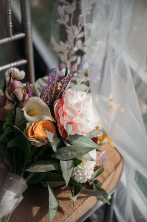 Wedding bouquet with peach roses, calla lilies and purple flowers against white tulle.