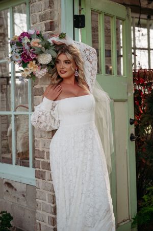 A bride with a floral bouquet stands beside a mint green door against a brick wall.