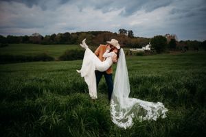 A couple shares a dramatic kiss in a green field with flowing veil and moody sky.