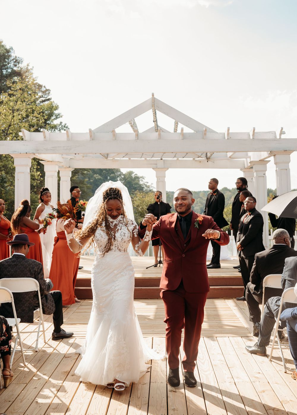 A celebratory wedding exit under a white pergola with guests in orange dresses.