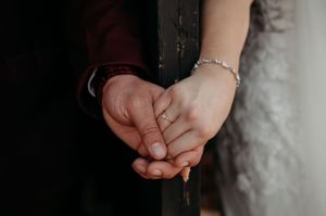 Close-up of clasped hands wearing a delicate bracelet against a dark background.