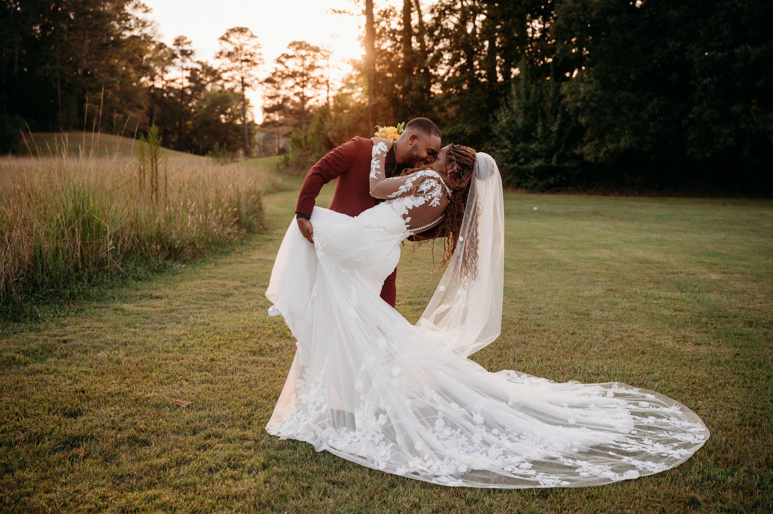A dramatic sunset wedding photo with flowing veil in an open field.