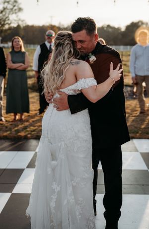 A couple embraces during an intimate dance moment on a checkered outdoor dance floor at sunset.