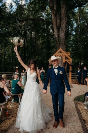 Newlyweds celebrate joyfully after ceremony under wooden arch with guests cheering.