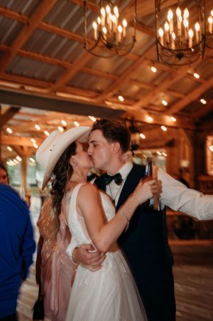 Romantic dance moment under warm barn lighting with cowboy hat and formal attire.