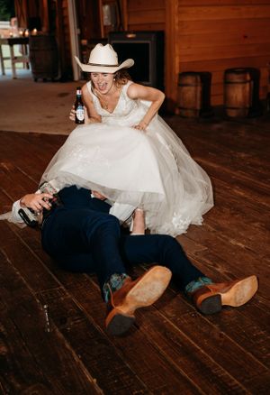 Playful wedding moment on wooden dance floor with cowboy boots and white hat.