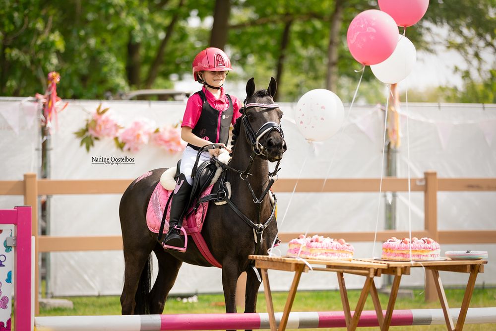 Pink balloons decorate an equestrian event with riders performing on horseback.