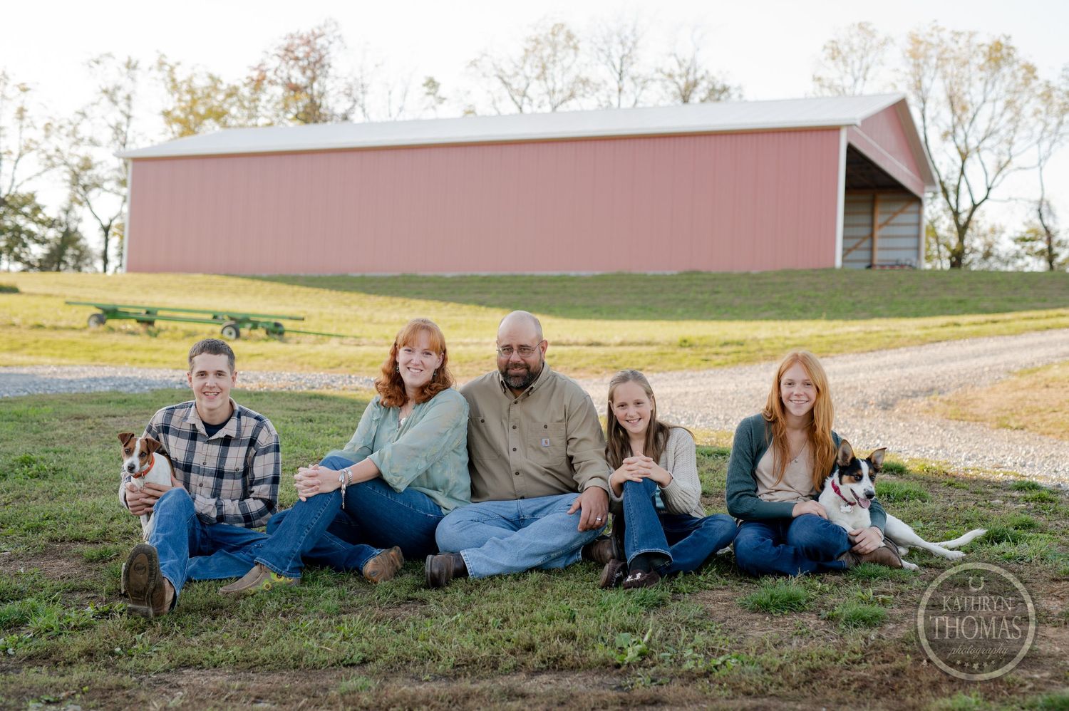 Family poses casually with their pets in front of a rustic pink barn.