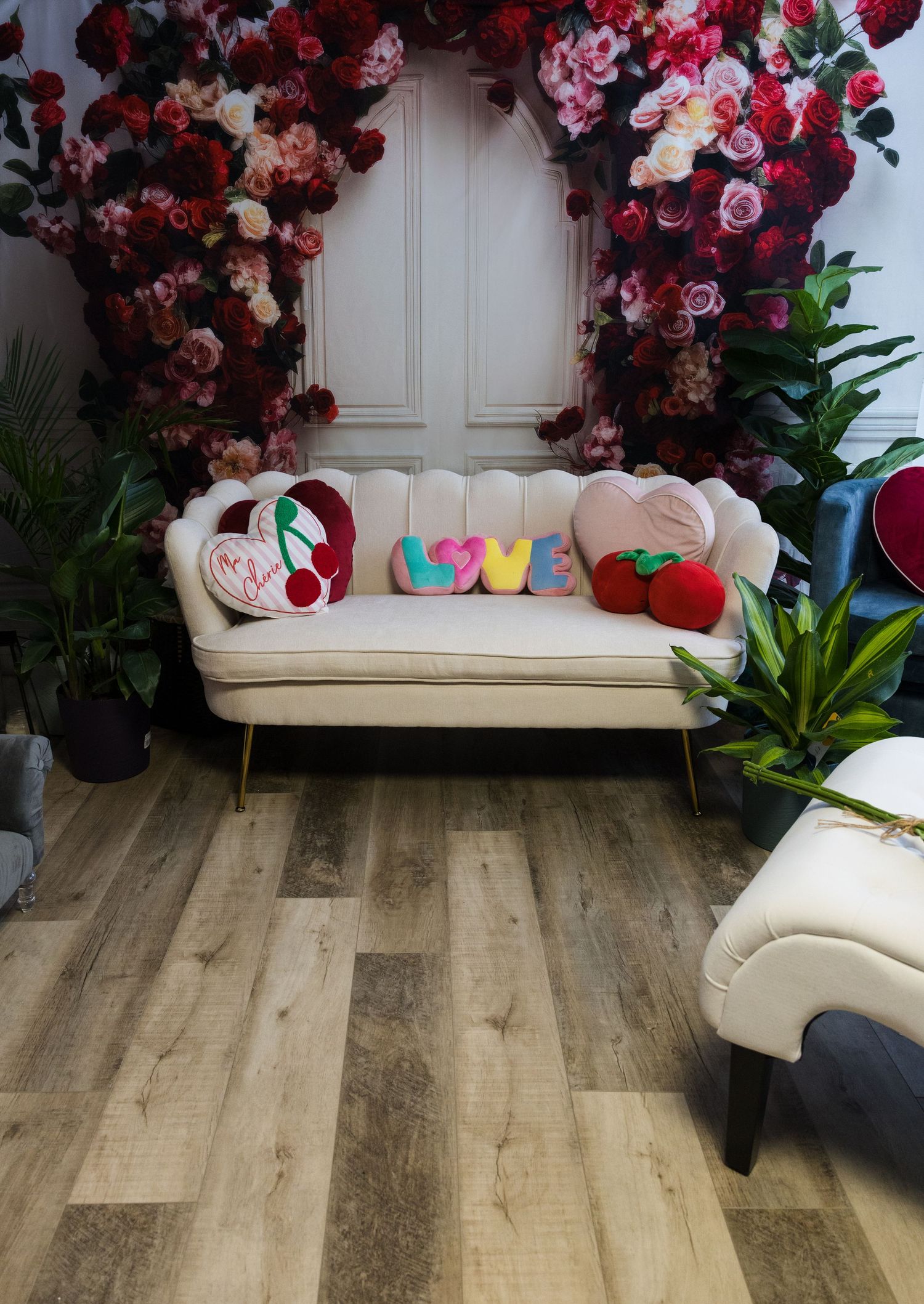 Elegant cream scallop sofa with colorful LOVE pillows surrounded by lush red and pink floral wall decor.