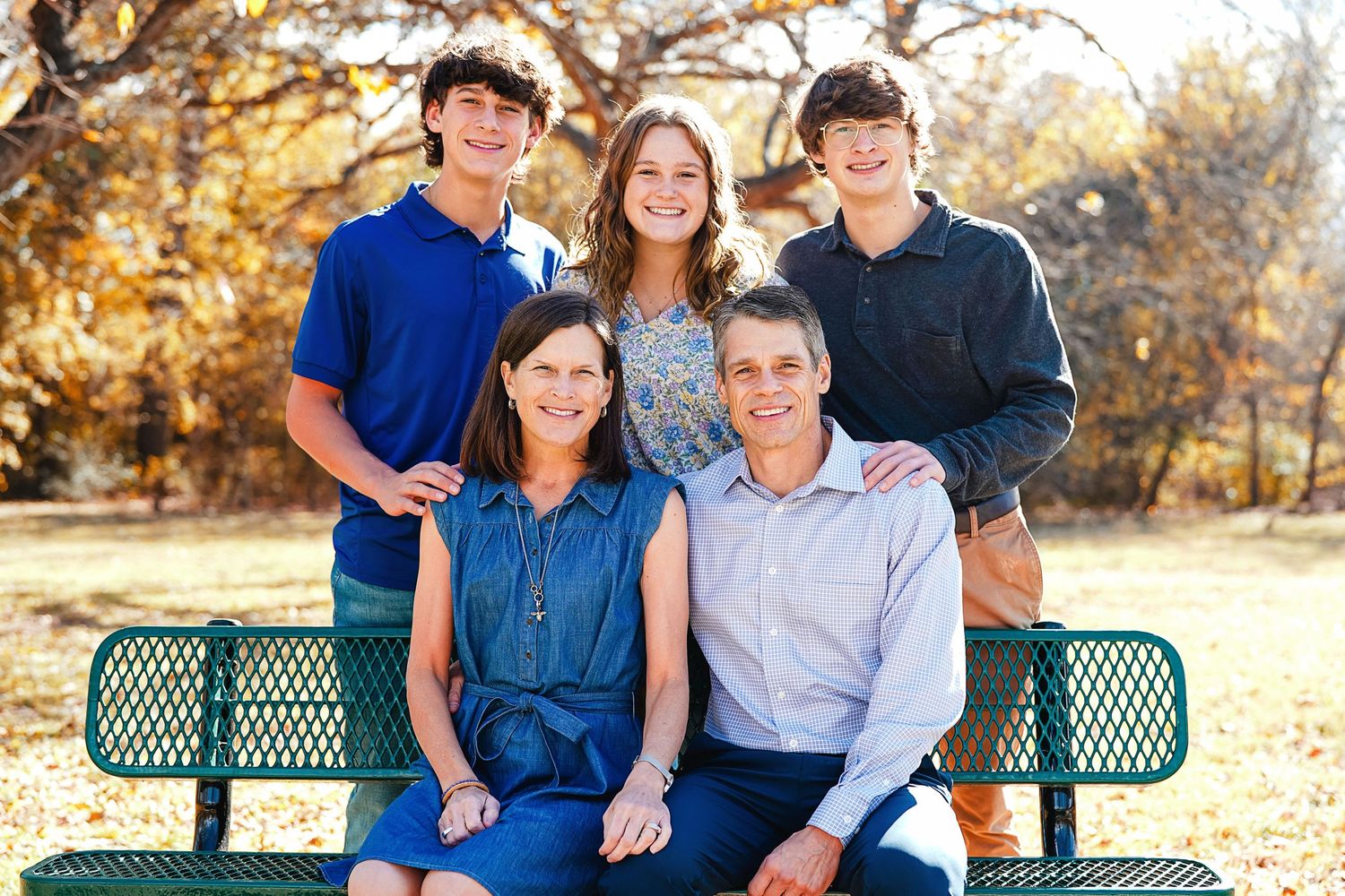 Family group sitting together on green park bench during fall season.
