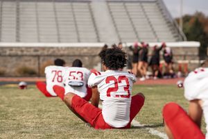 Athletes in red and white uniforms stretch on a football field before a game.