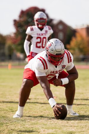 A football player in red and white uniform crouches with the ball during practice.