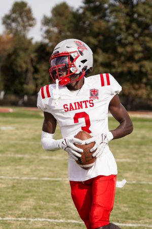 Football player in white and red Saints uniform carrying ball on field during game.
