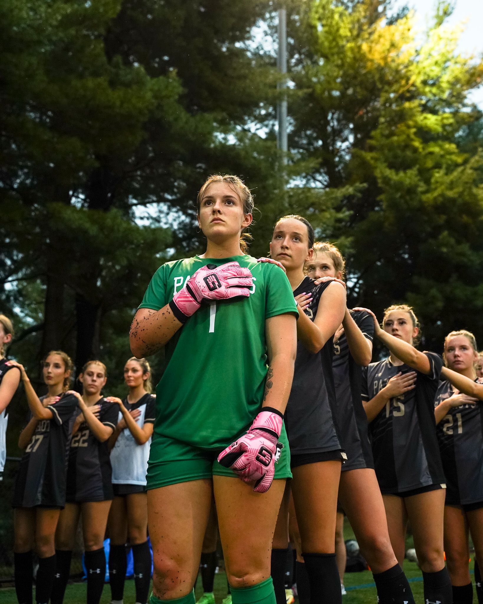Soccer team members in green and black uniforms stand in formation on grass field.