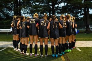 Soccer team huddles together wearing matching black uniforms and knee-high socks.