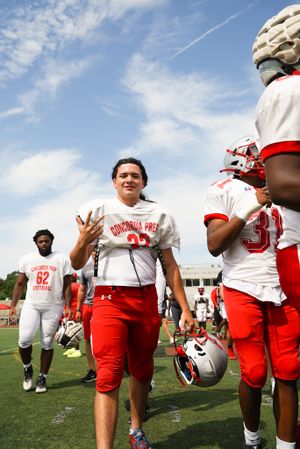 Football players and coach interact on field during practice session.