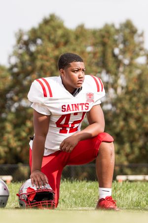Saints football player in white jersey number 42 kneels on field with helmet.
