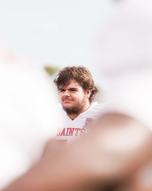 Football player in a white Saints jersey gazes upward during a sunny day on the field.