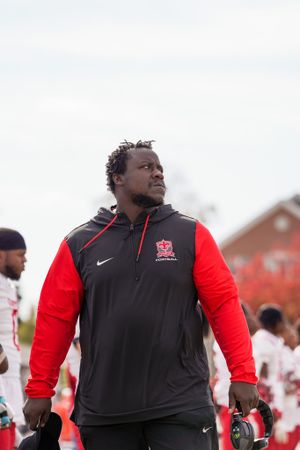 Coach in black and red Nike Saints gear stands on sideline during game.