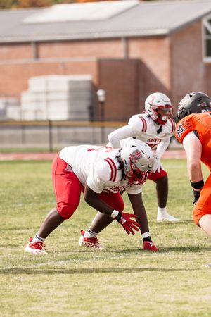 Football players in white and orange uniforms line up at scrimmage during game play.