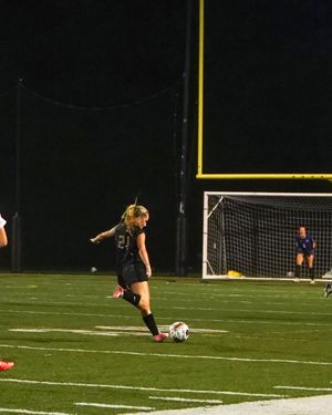 Soccer player prepares to kick ball during nighttime match under stadium lights.