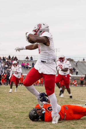 Saints player in white uniform leaps over defender in orange during football game action.