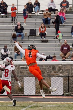 Football player in orange jersey makes an athletic leaping catch during game with spectators watching from bleachers.