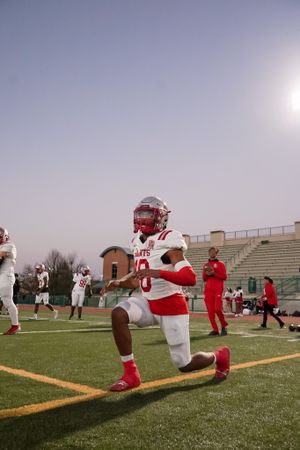 Football player stretches during warmup drills on field with stadium bleachers in background.