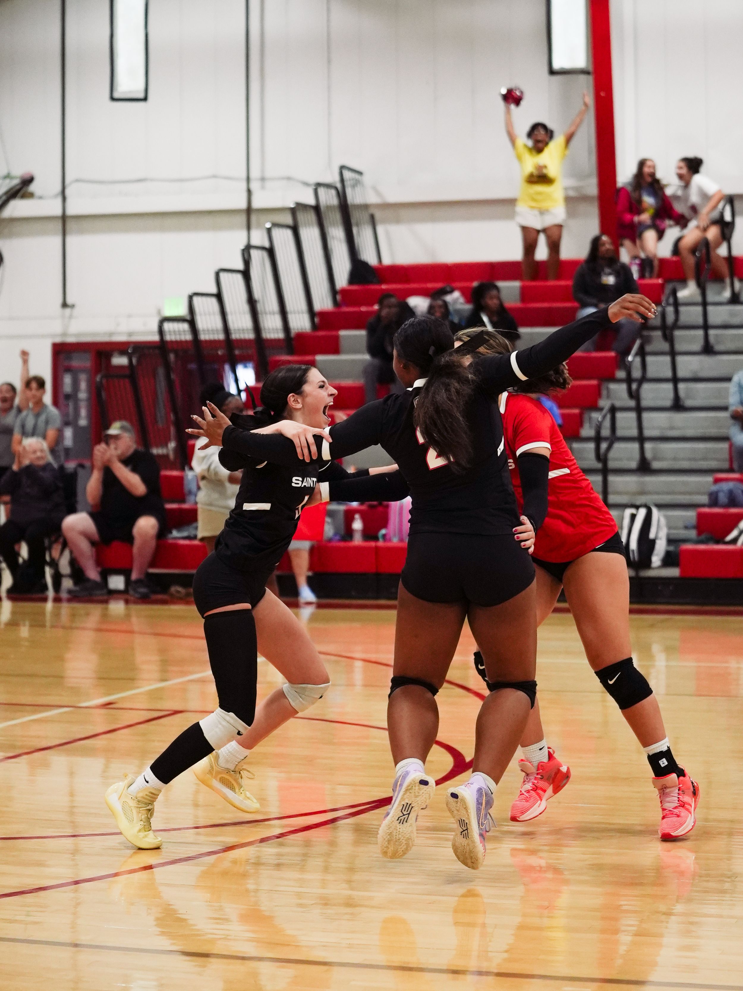 Volleyball players in black uniforms perform a synchronized diving drill during practice on a gymnasium court.