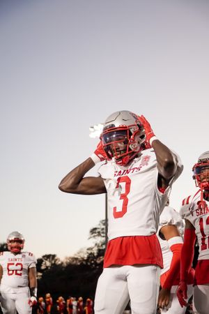 Football player in white uniform with red accents poses during sunset.