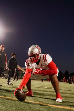 Football player crouches with ball on field during nighttime game.