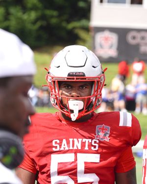 Football player wears red Saints jersey with matching helmet and facemask.