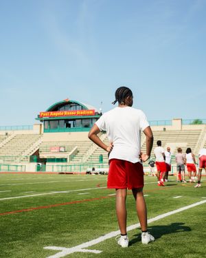 Player stands on football field with stadium press box visible in background.