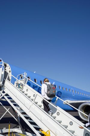 Person climbing airplane boarding stairs with blue aircraft fuselage visible.